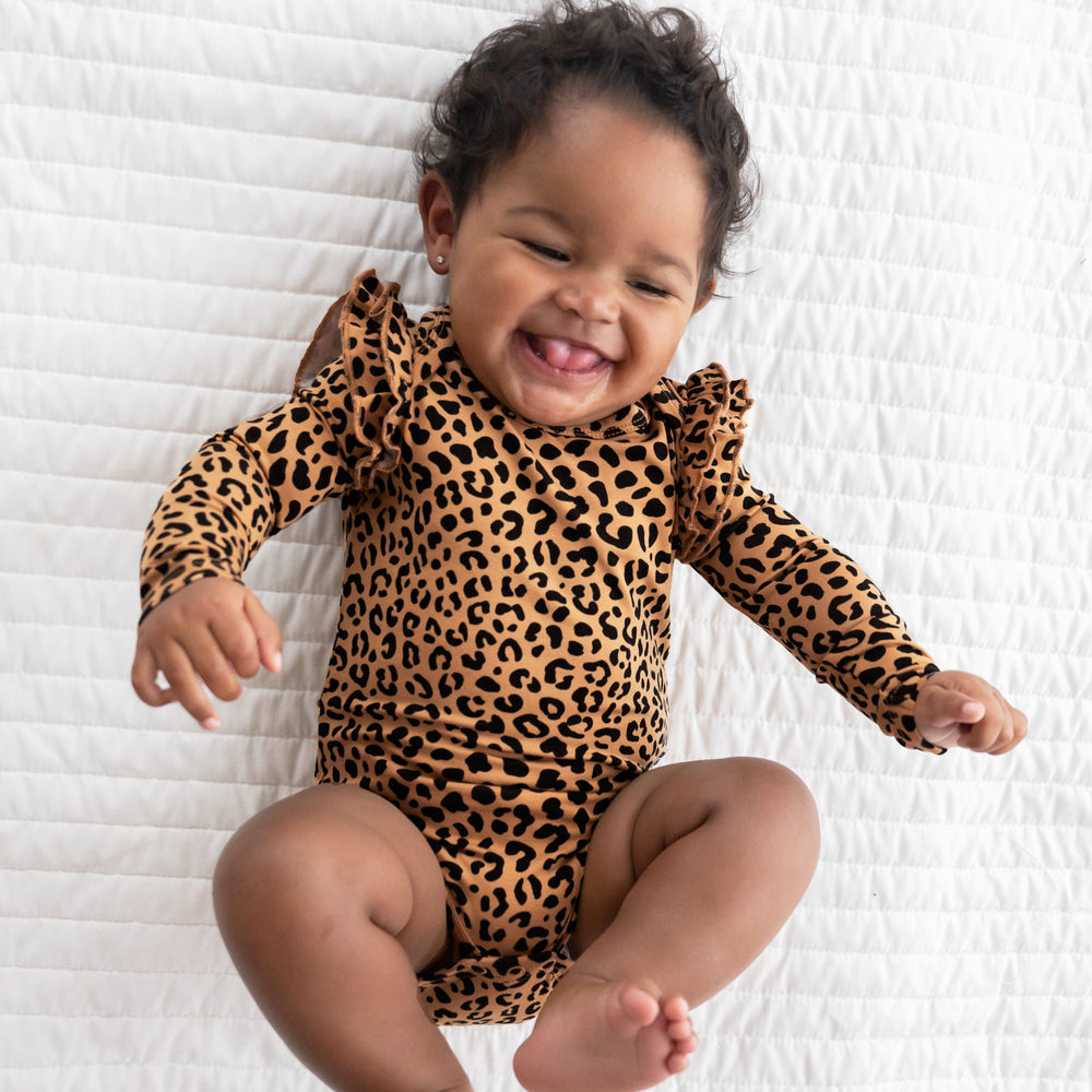 Top view image of baby laying down and smiling while in the Classic Leopard Flutter Bodysuit