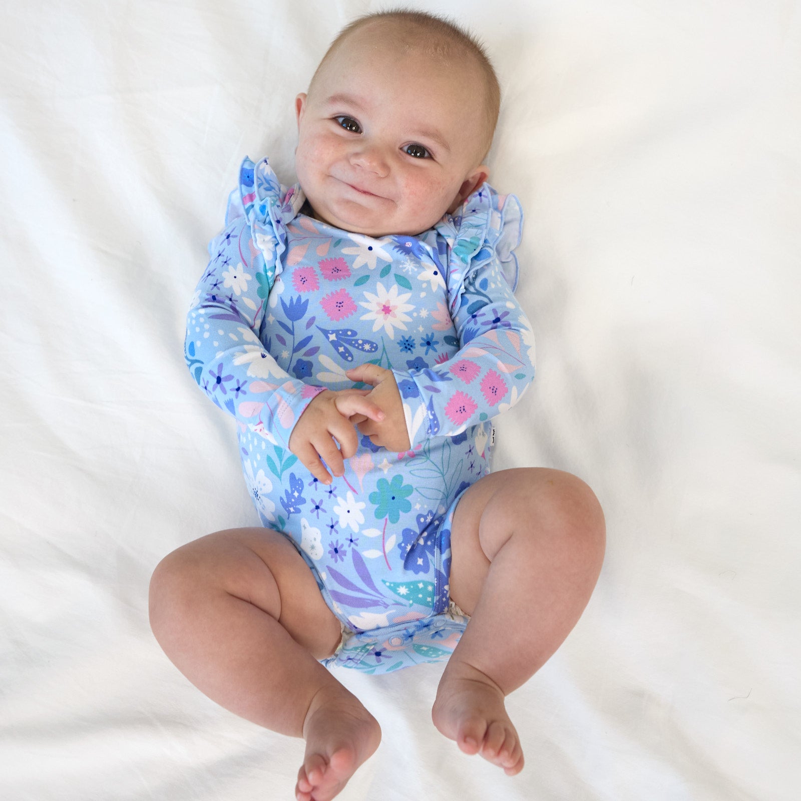 Top view image of baby laying down while wearing the Magical Meadow Flutter Bodysuit