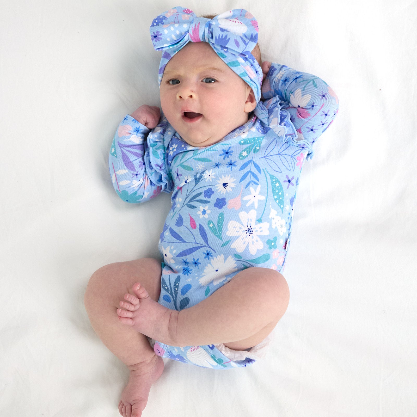 Top view image of the baby laying down in the Magical Meadow Flutter Bodysuit and Magical Meadow Luxe Bow