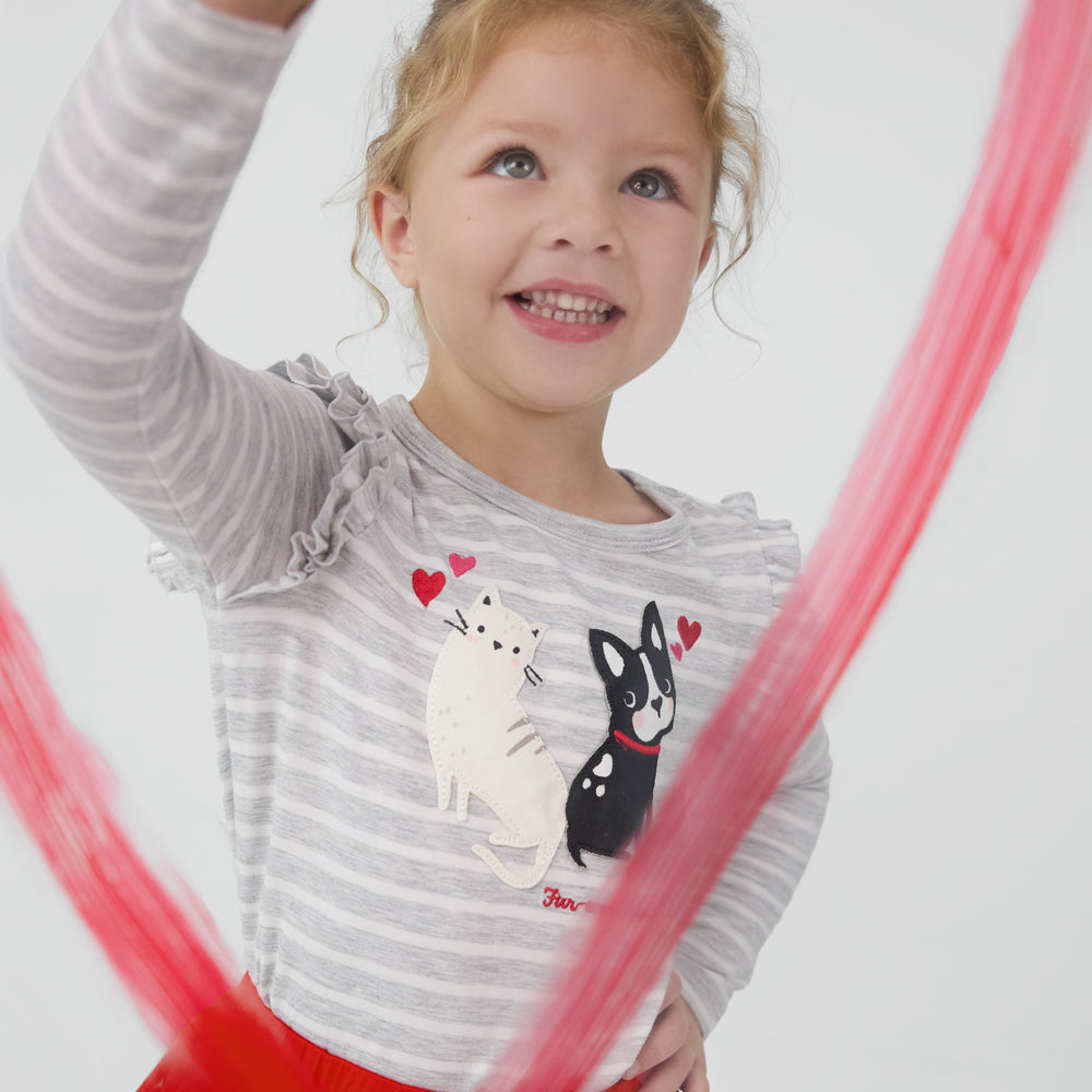 Smiling child drawing a heart and wearing a Furever Friends Flutter Tee