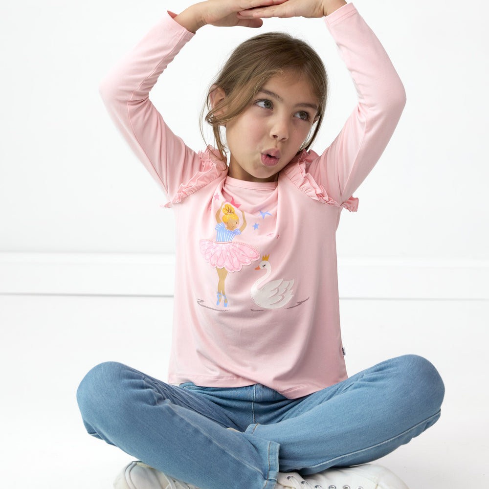 Girl sitting while posing in the Prima Pink Flutter Tee and Light Blue Denim Leggings