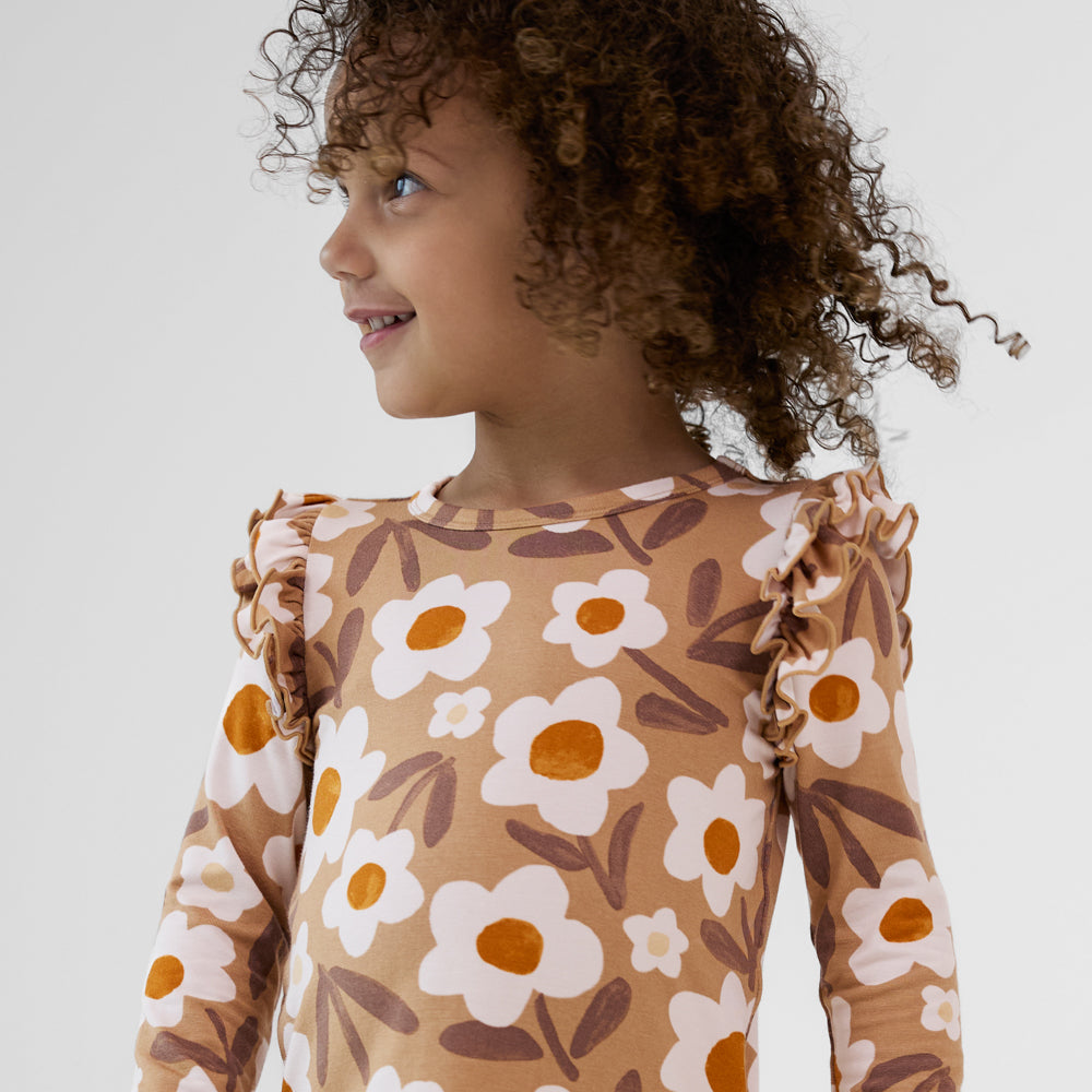 Child looking to the side wearing a Daisy Daydream flutter tee with ruffle shoulders, long sleeves, and a tan floral design