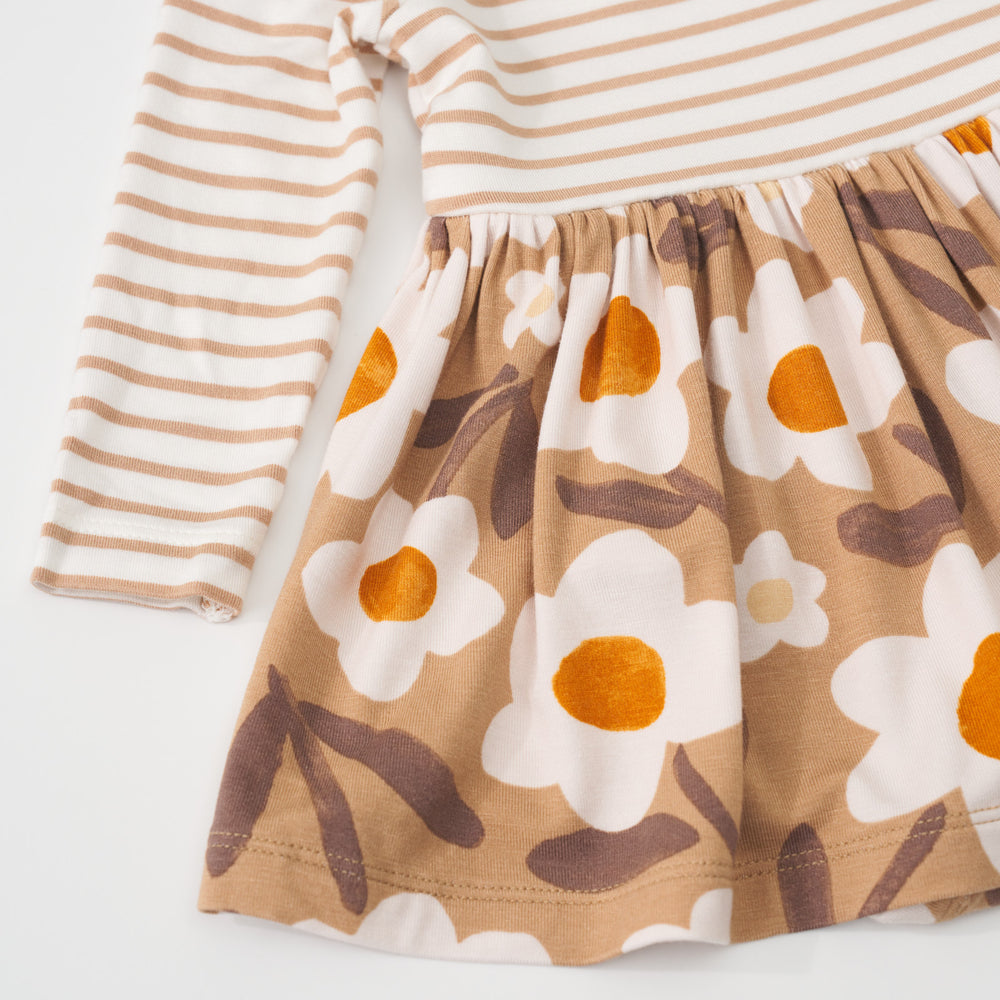 Close up view of the tan stripes top pattern and tan floral skirt pattern on a Daisy Daydream twirl dress with bodysuit