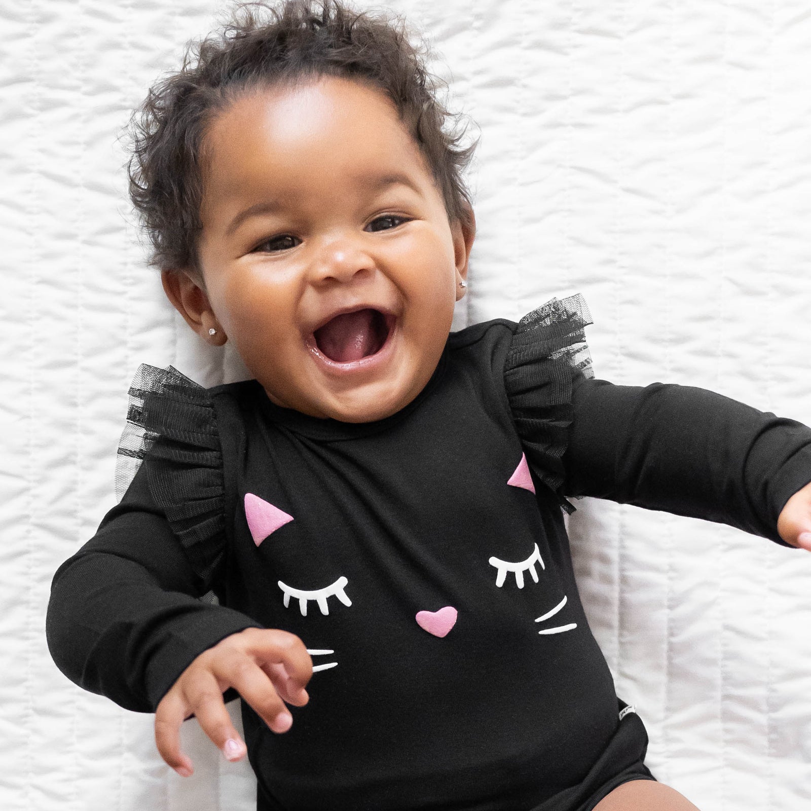 Top view close up image of baby laying down while in the Black Cat Graphic Flutter Bodysuit