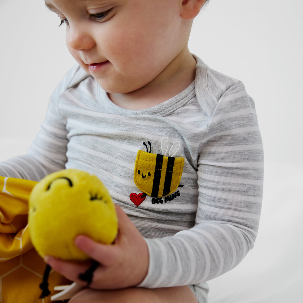 close up view of a child wearing a bee mine pocket bodysuit holding a honey the bee sleepyhead lovey