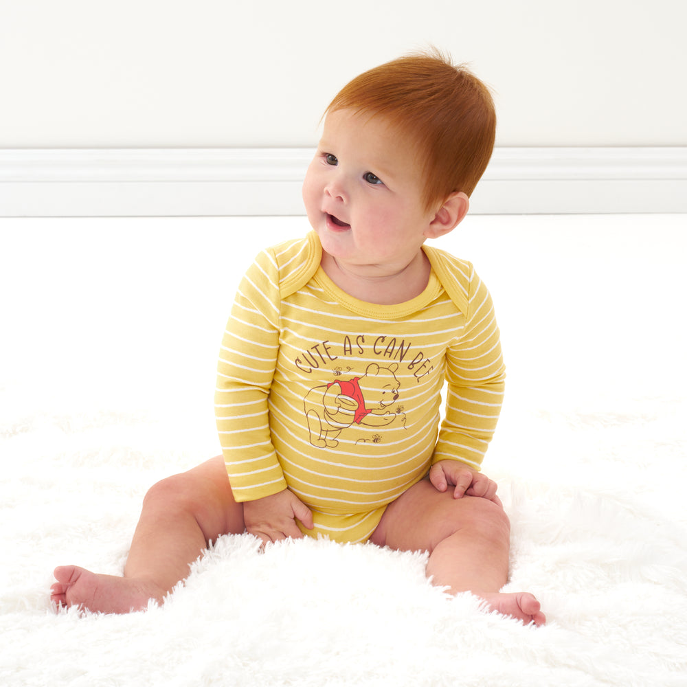 Click to see full screen - Child sitting on a blanket wearing a Disney Winnie the Pooh graphic bodysuit
