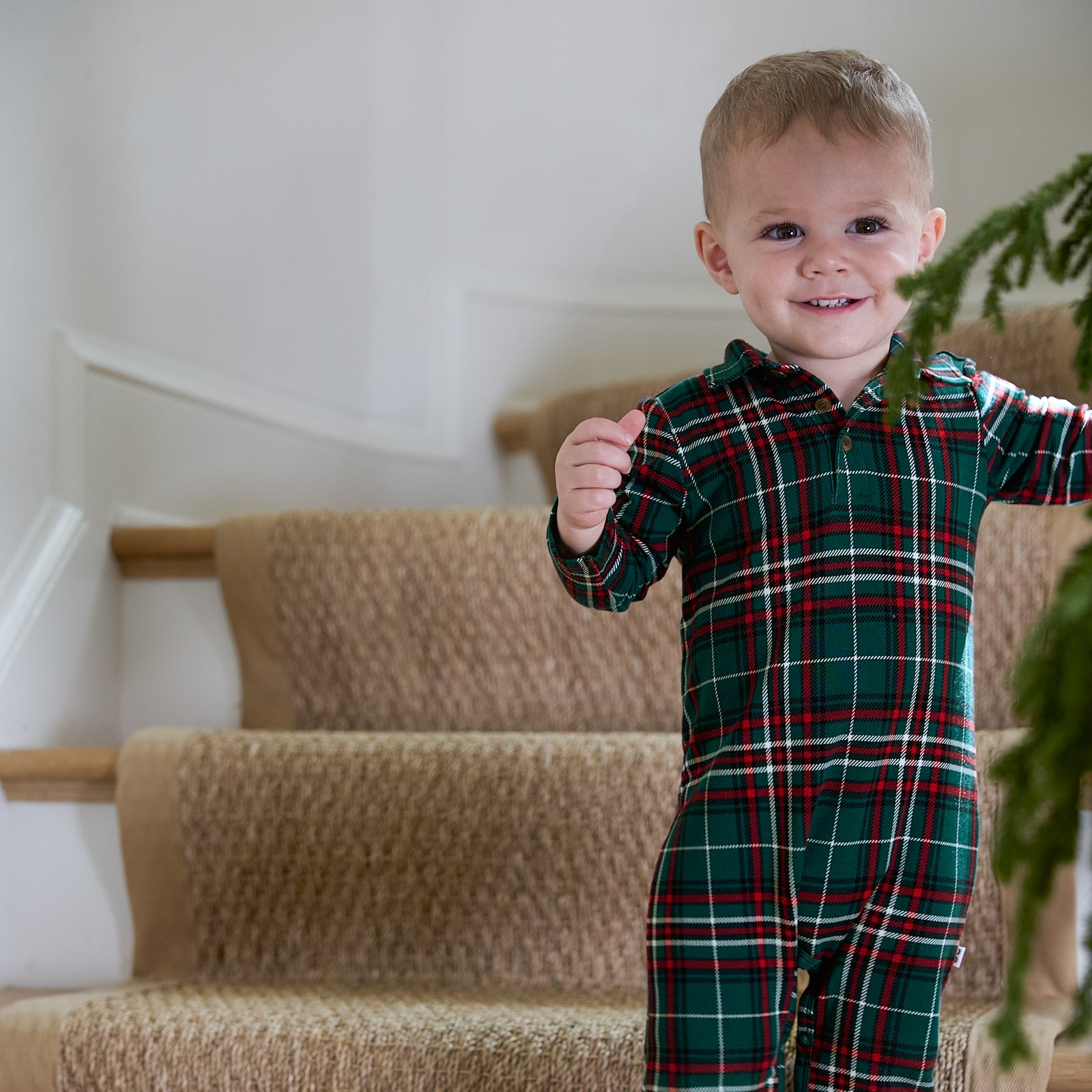 Image of a child standing on the stairs wearing an Evergreen Plaid Polo Romper