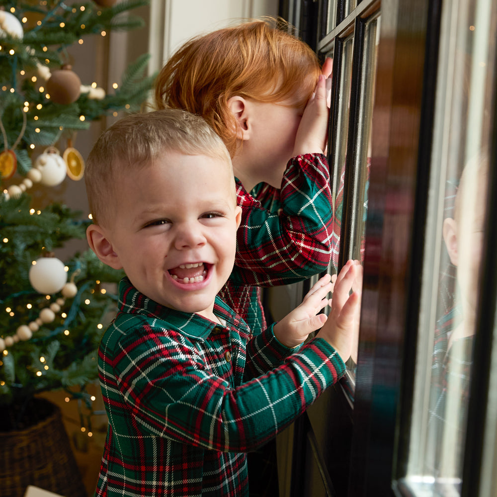 Two children looking out a window wearing coordinating Holiday plaid Play styles