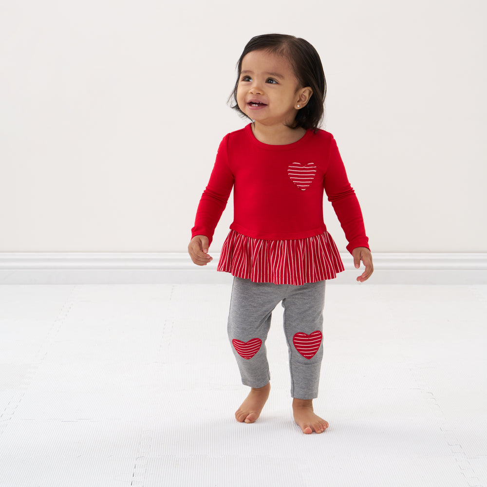 Click to see full screen - Child walking forward wearing a Candy Red peplum tee and coordinating heart patch leggings