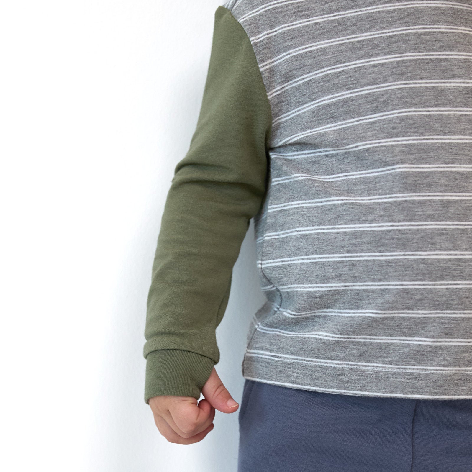 Close up detail shot of a boy wearing a Light Heather Gray Stripes Hooded Tee, detailing the thumbhole on the sleeve cuff.