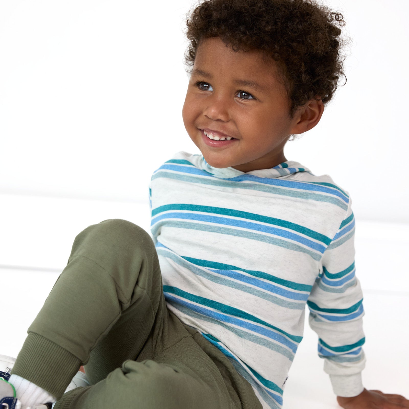 Additional image of smiling boy sitting while wearing the Cool Stripes Relaxed Hooded Tee and Moss Jogger