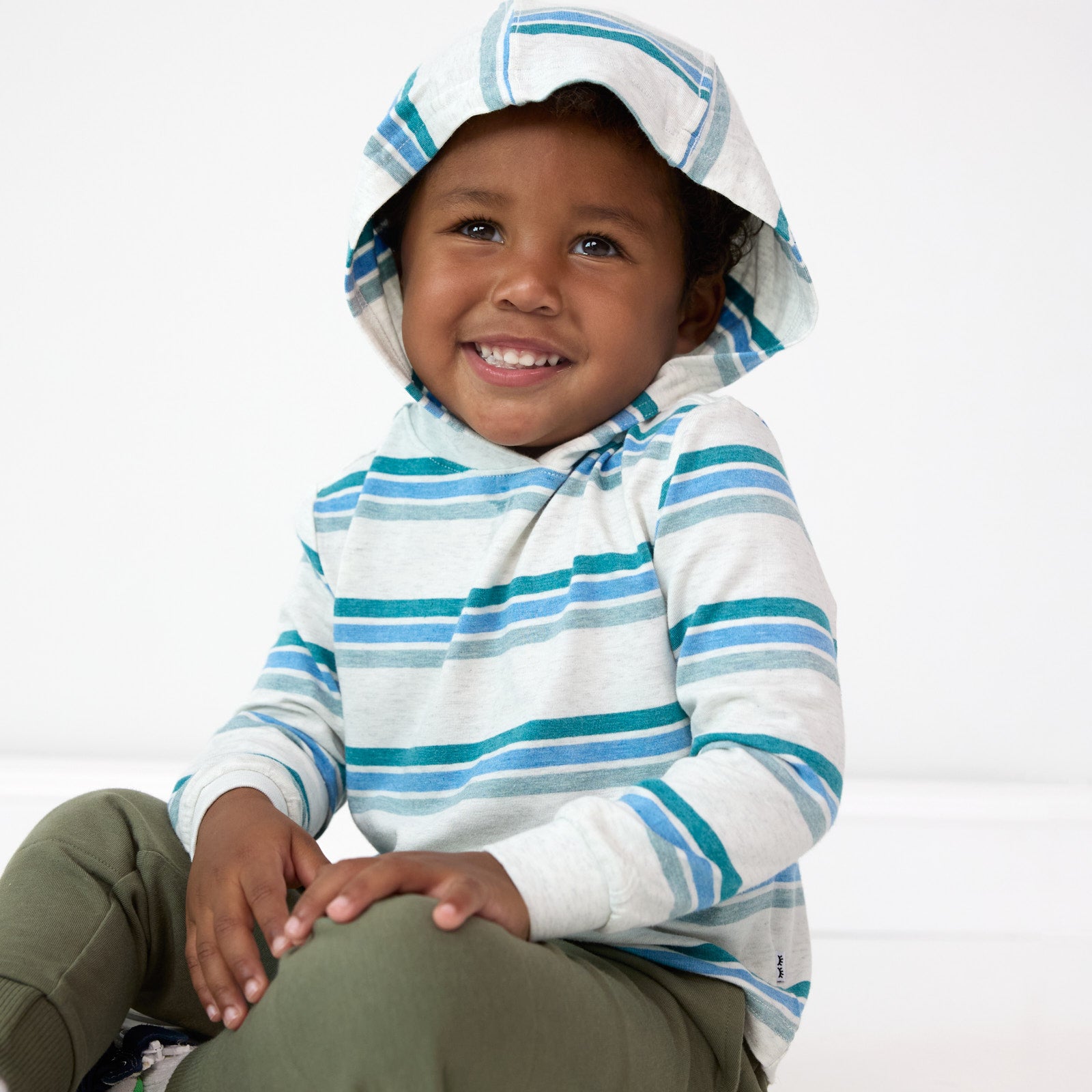 Smiling boy sitting down wearing the Cool Stripes Relaxed Hooded Tee displaying the hood feature