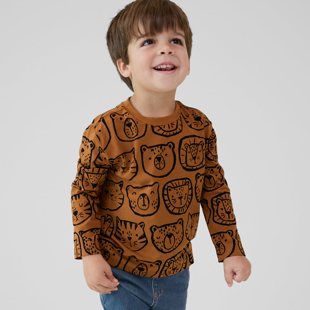 Smiling child wearing an Amber Lions, Tigers & Bears Relaxed Tee with black animal illustrations, paired with denim joggers.