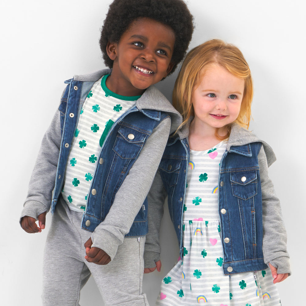 Click to see full screen - Two children posing together. One is wearing Lucky in Love skater dress paired with a denim jacket. The second child is wearing a Lucky Stripes pocket tee paired with a denim jacket and coordinating heather gray joggers.
