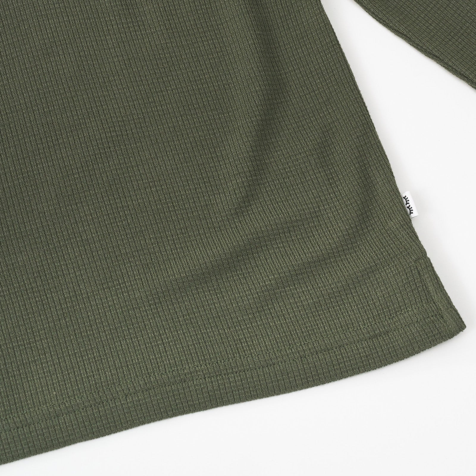 Close up detail shot of an Olive Waffle Henley Tee, showing the Sleepy Eyes logo tag