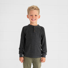 Close up image of a child wearing a Heather Black Waffle Henley Tee and Olive Denim Jogger