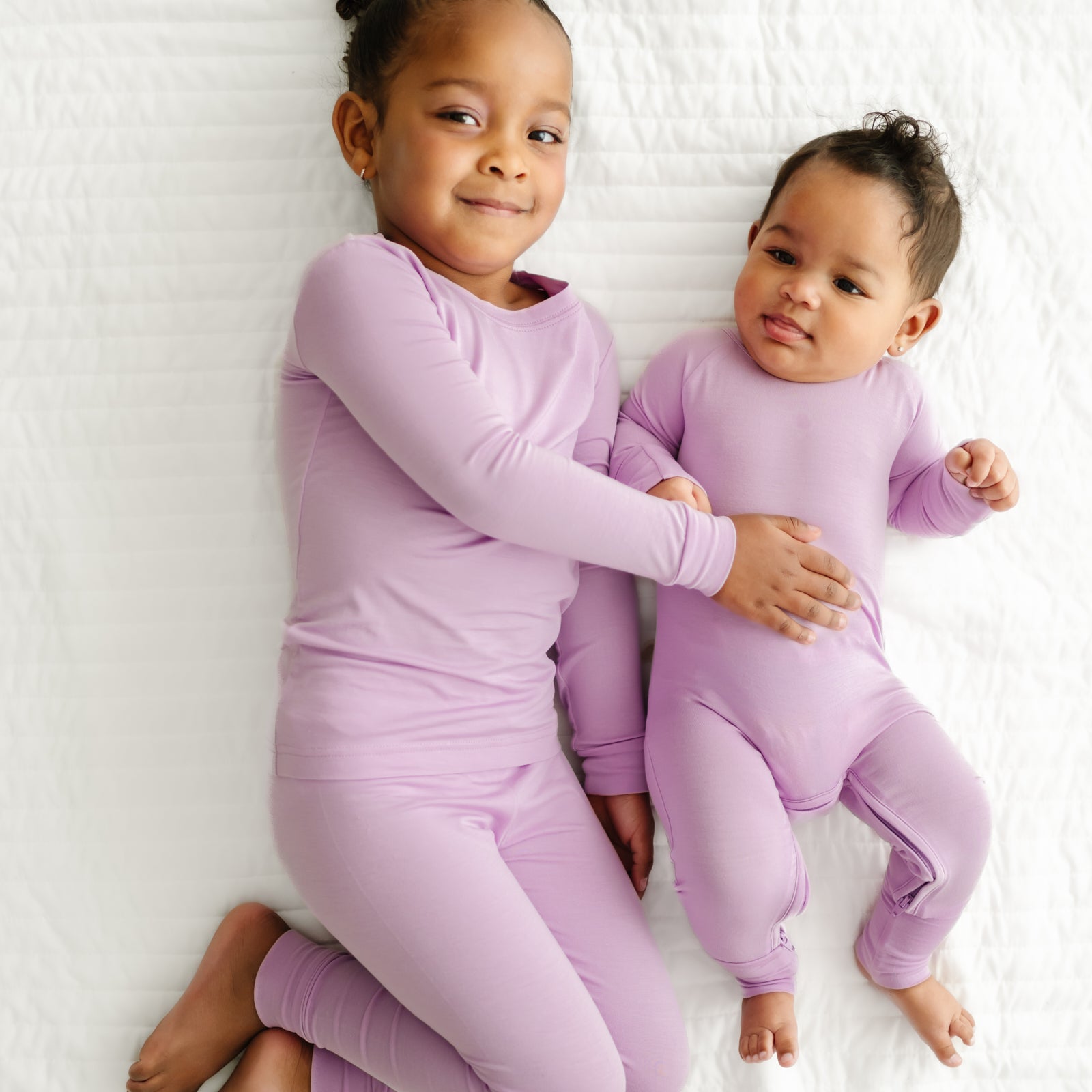 Two children cuddling wearing matching Light Orchid two piece pajama sets in two piece and crescent zippy styles