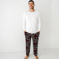 Image of a man wearing men's Black XOXO pajama pants paired with a solid white men's pajama top