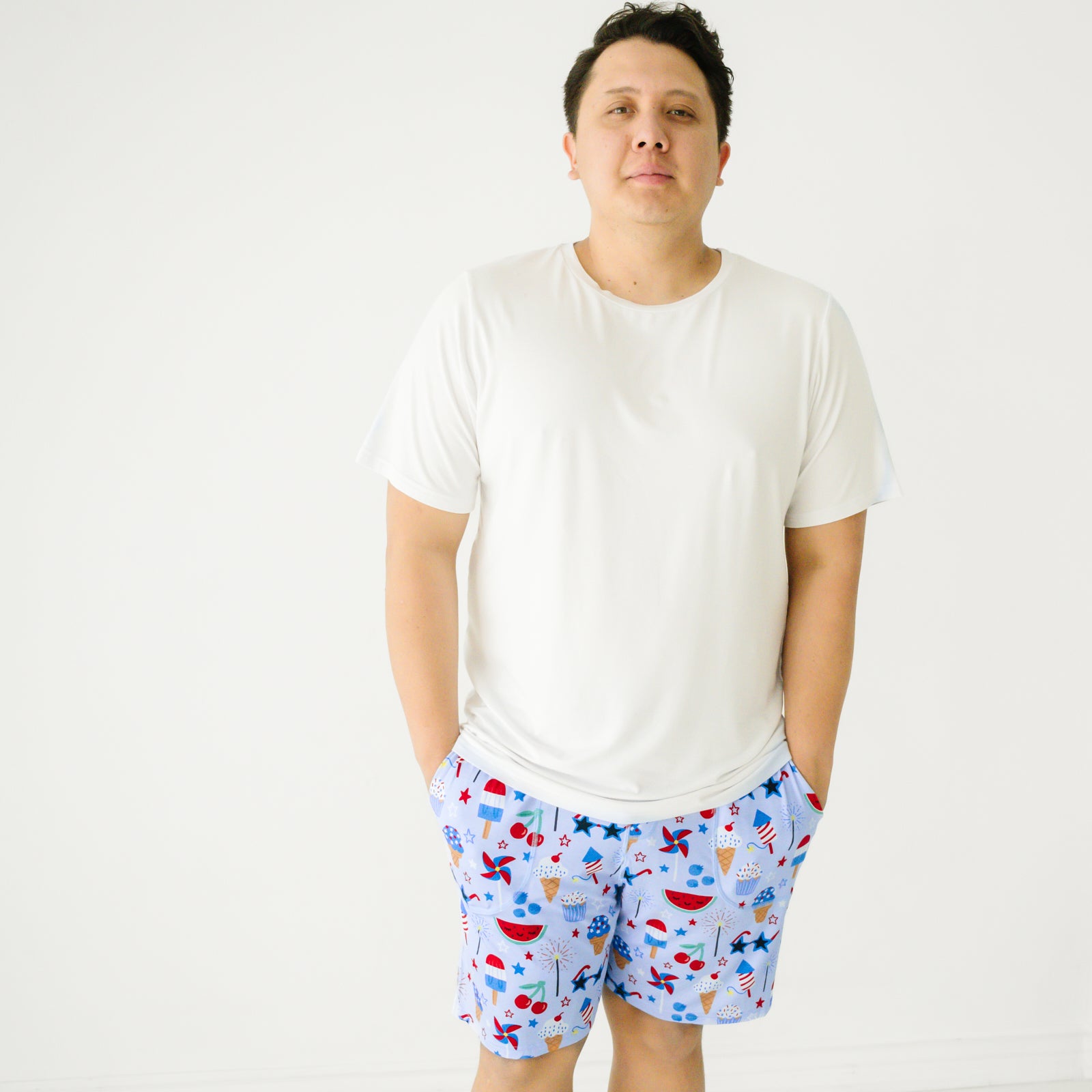 Close up image of a man wearing Stars Stripes and Sweets printed men's pj shorts paired with a men's bright white pj top