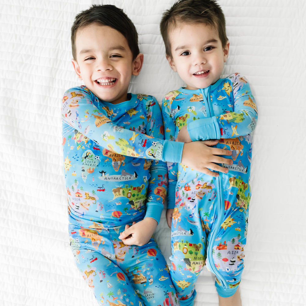 Two children laying on a bed together wearing matching Around the World pajamas in zippy and two piece pajama set styles