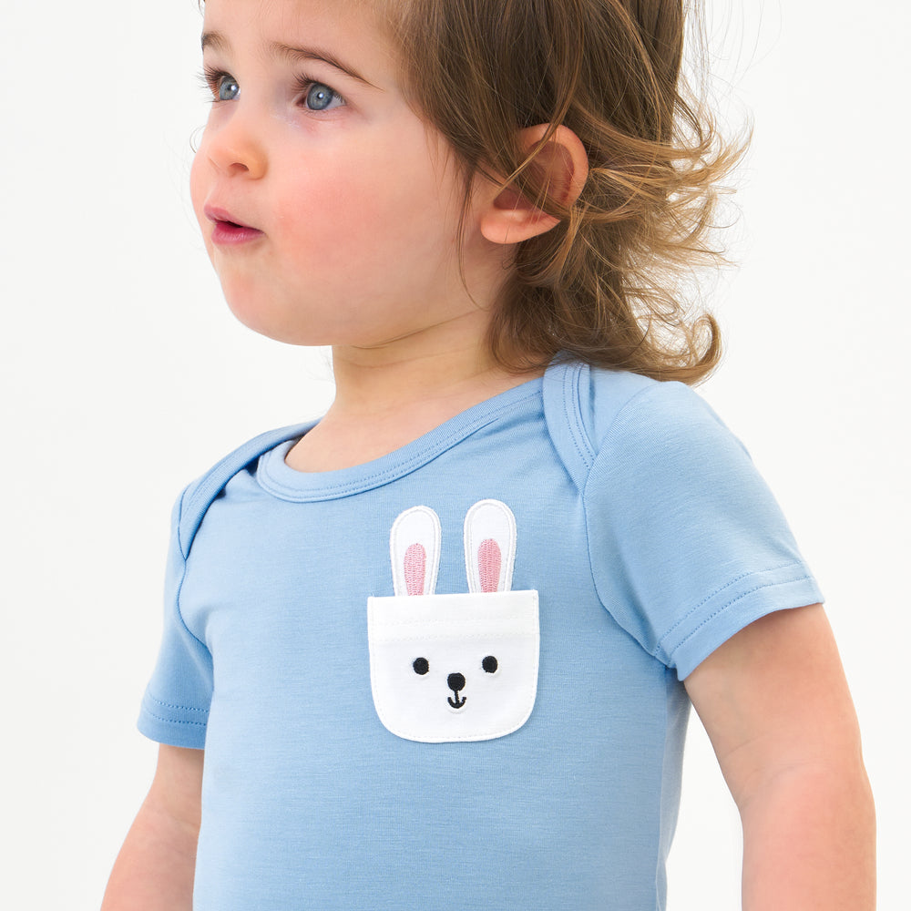 Close up image of a child wearing a Lake Blue pocket bodysuit detailing the pocket