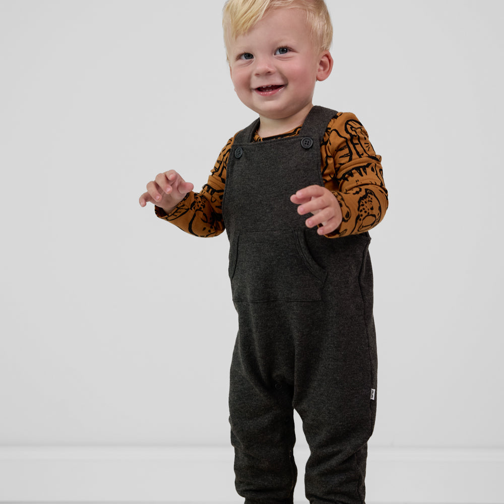 Child wearing a Heather Black overall paired with an amber with black animal print long sleeve baby bodysuit