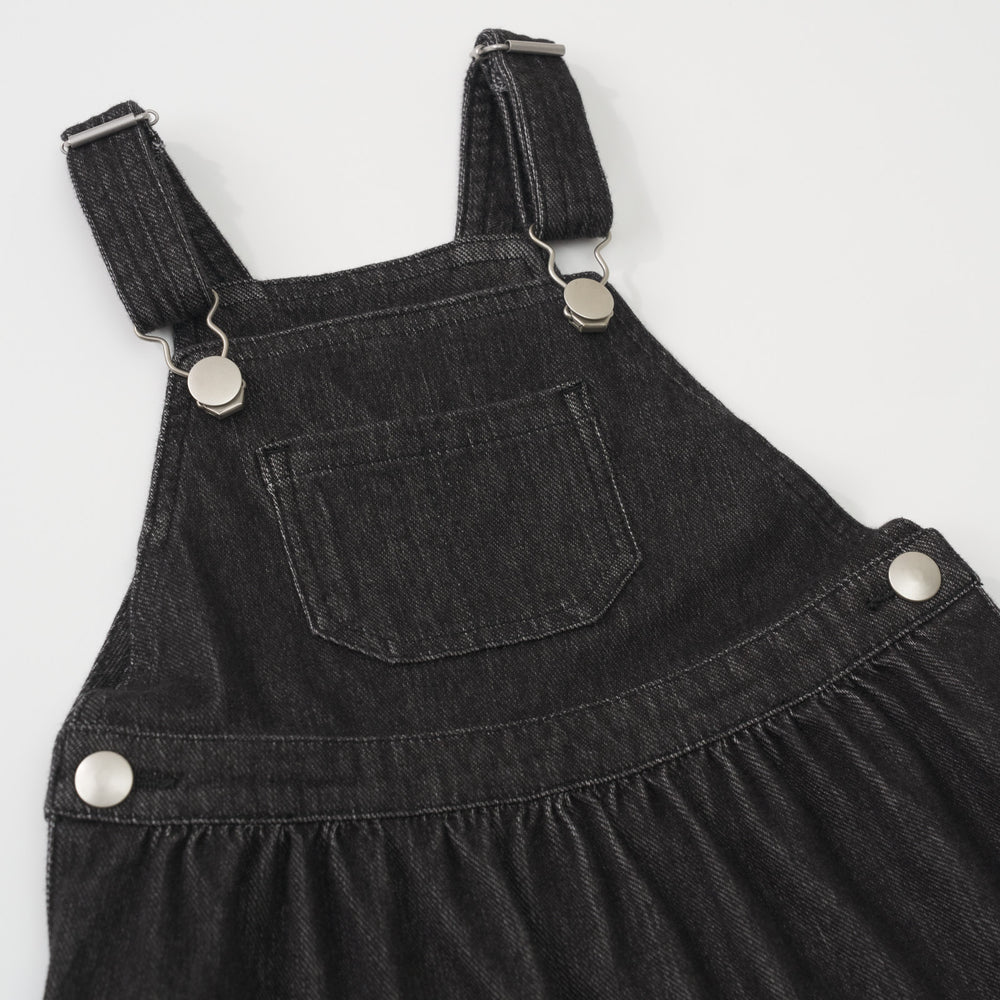 Close-up view of the front pocket and silver buckles on a Black denim tank skirt overall