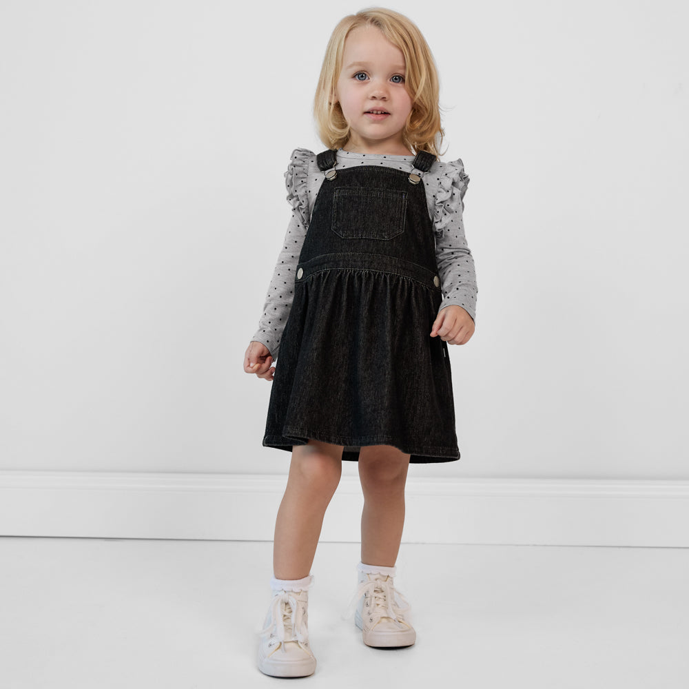 Child wearing a Black denim tank skirt overall paired with a gray ruffle shoulder long sleeve top