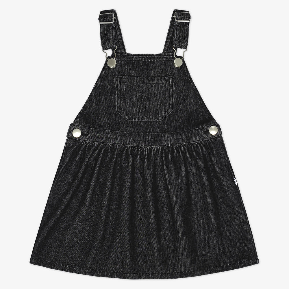 Flat lay of a Black denim tank skirt overall with a front pocket and silver buckles