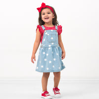 Child wearing a Candy Red Stripes flutter tee and coordinating Play overalls and luxe bow headband