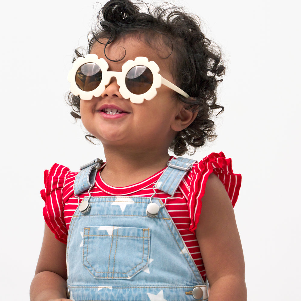 Close up image of a child wearing a Denim Stars tank skirt overall, coordinating bodysuit, and sunglasses