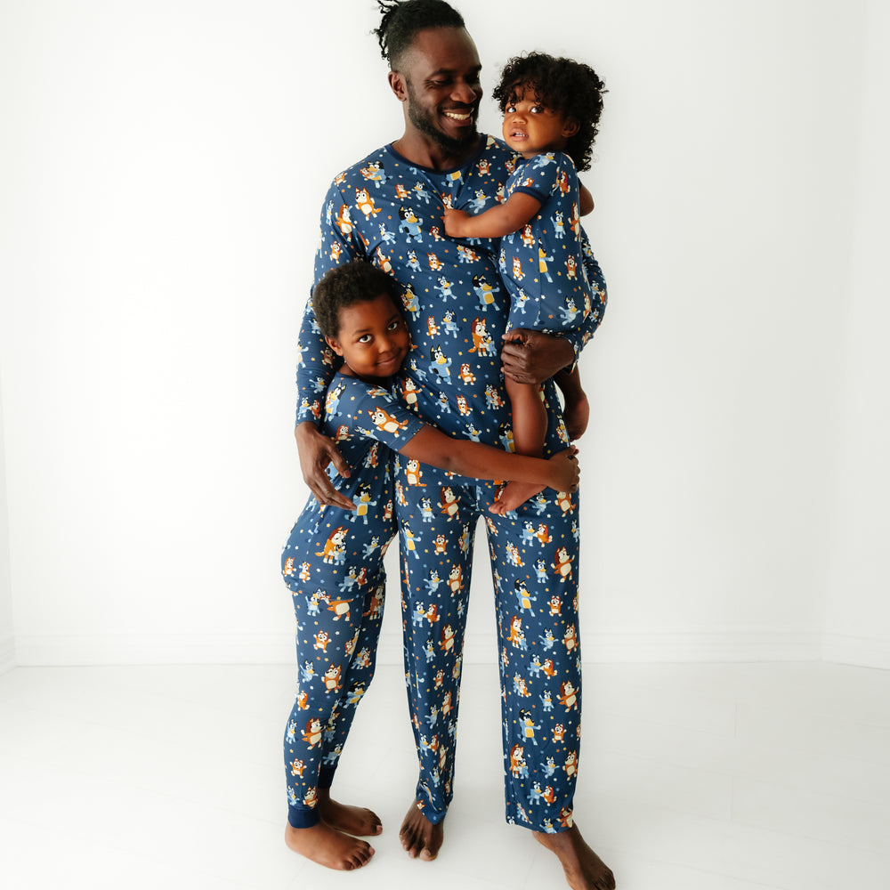 Father and his two children matching wearing Bluey Dance Mode pajamas. Dad is wearing men's Bluey Dance Mode men's pajama top and matching men's pajama pants. Children are matching wearing Bluey Dance Mode short sleeve two piece pajama set and shorty zippy