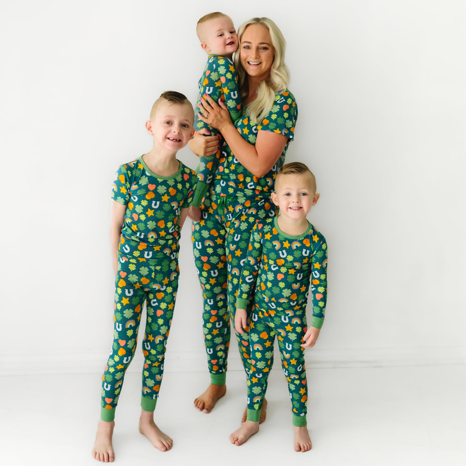Mother and her three sons wearing matching Lucky printed pajama sets. Mom is wearing women's Lucky printed pajama top and matching pajama pants. Her children are wearing Lucky printed pajamas in short sleeve two piece, long sleeve two piece, and zippy styles.