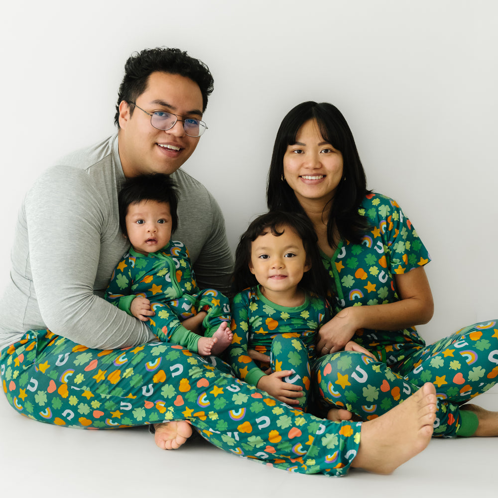 Click to see full screen - Family of four sitting together wearing matching Lucky printed pajamas. Dad is wearing a men's solid Heather Gray pajama top and Lucky printed men's pajama pants. Mom is wearing a women's Lucky printed pajama top and matching pajama pants. Their children are matching wearing Lucky printed two piece pajama set and zippy.