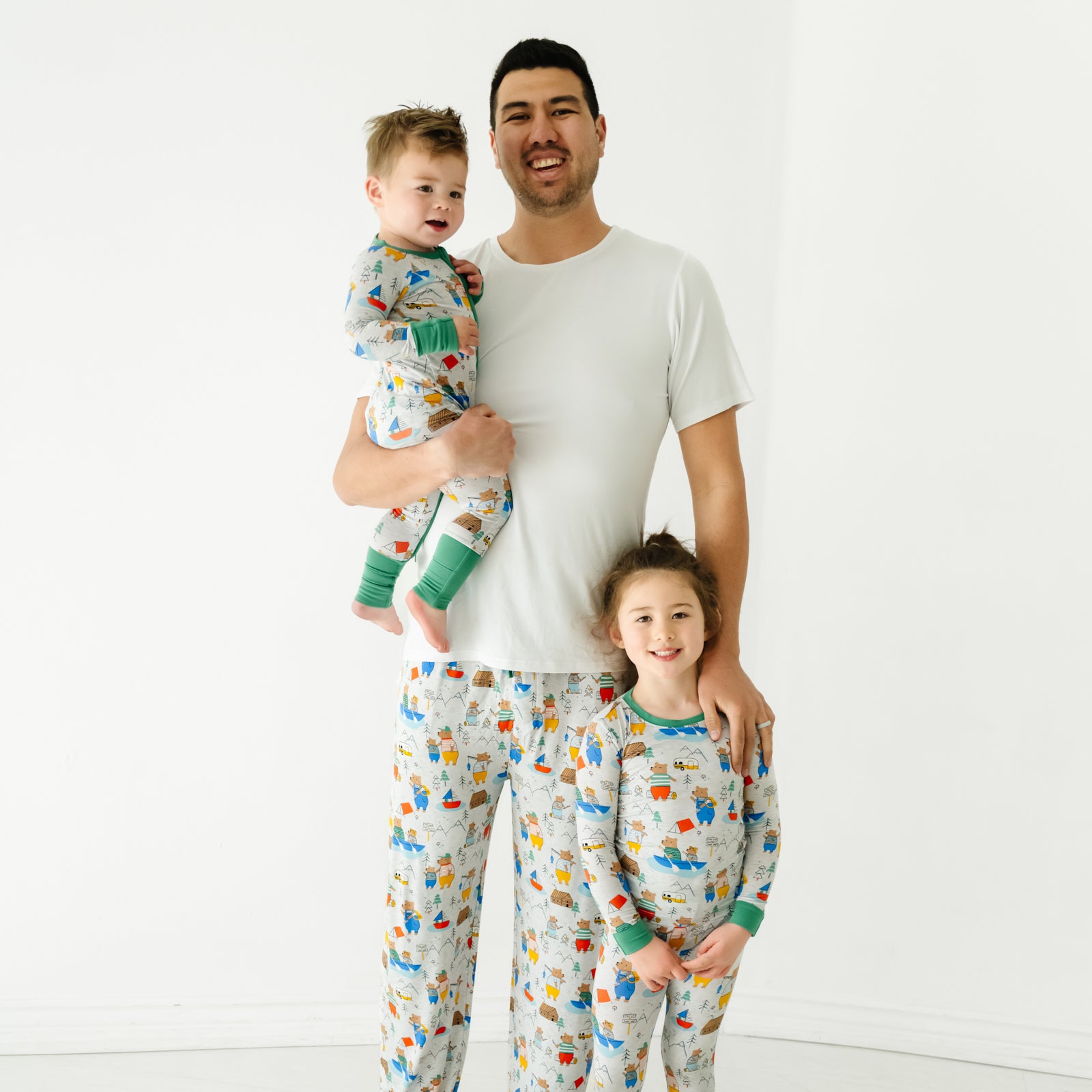 father and children posing together. Dad is wearing a men's bright white pajama top and men's Papa Bear pajama pants. Kids are wearing matching Papa Bear printed pajamas in zippy and two piece styles