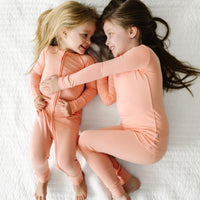 two children cuddling together wearing matching Peach pjs in zippy and two piece styles