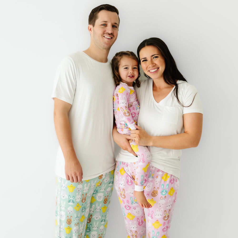 Click to see full screen - Family of three posing together. Dad is wearing men's Aqua Pastel Parade pajama pants paired with a men's Bright White short sleeve pajama top. Mom is wearing Pink Pastel Parade women's pajama pants paired with a coordinating Bright White women's pocket tee. Her daughters is matching wearing a Pink Pastel Parade two piece pajama set