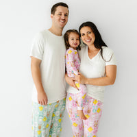 Family of three posing together. Dad is wearing men's Aqua Pastel Parade pajama pants paired with a men's Bright White short sleeve pajama top. Mom is wearing Pink Pastel Parade women's pajama pants paired with a coordinating Bright White women's pocket tee. Her daughters is matching wearing a Pink Pastel Parade two piece pajama set