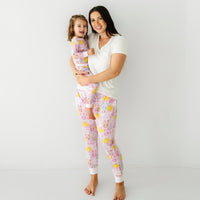 Mother holding her daughter up and posing together. Mom is wearing Pink Pastel Parade women's pajama pants paired with a coordinating Bright White women's pocket tee. Her daughters is matching wearing a Pink Pastel Parade two piece pajama set