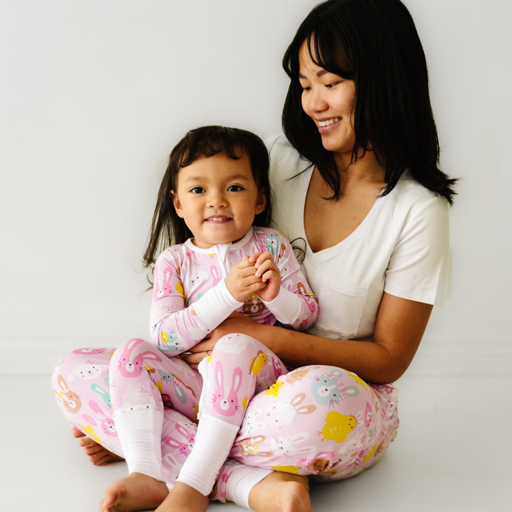 Click to see full screen - Mother and daughter sitting together. Mom is wearing Pink Pastel Parade women's pajama pants paired with a coordinating Bright White women's pocket tee. Her daughters is matching wearing a Pink Pastel Parade zippy