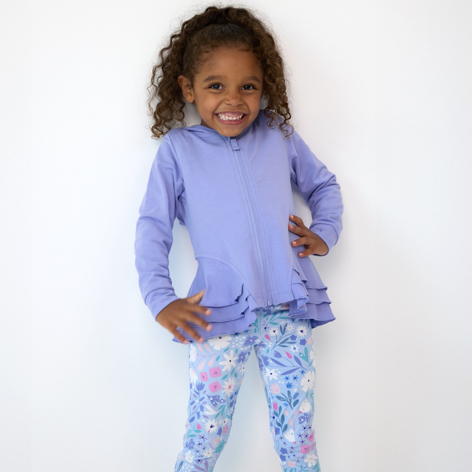 Smiling girl posing while wearing the Light Iris Peplum Hoodie and Magical Meadow Leggings