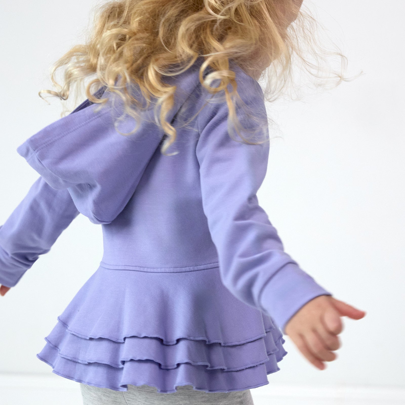 Image of girl twirling, featuring the back details on the Light Iris Peplum Hoodie