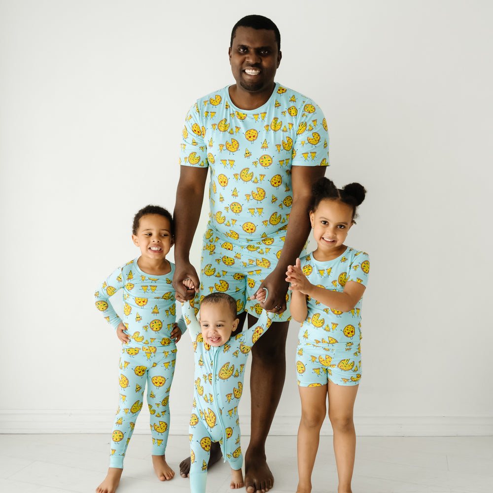 Dad and his three kids wearing matching Pizza Pals pjs. Dad is wearing men's Pizza Pals men's pj top and matching men's pj shorts. Kids are wearing matching Pizza Pals pjs in two piece and zippy styles