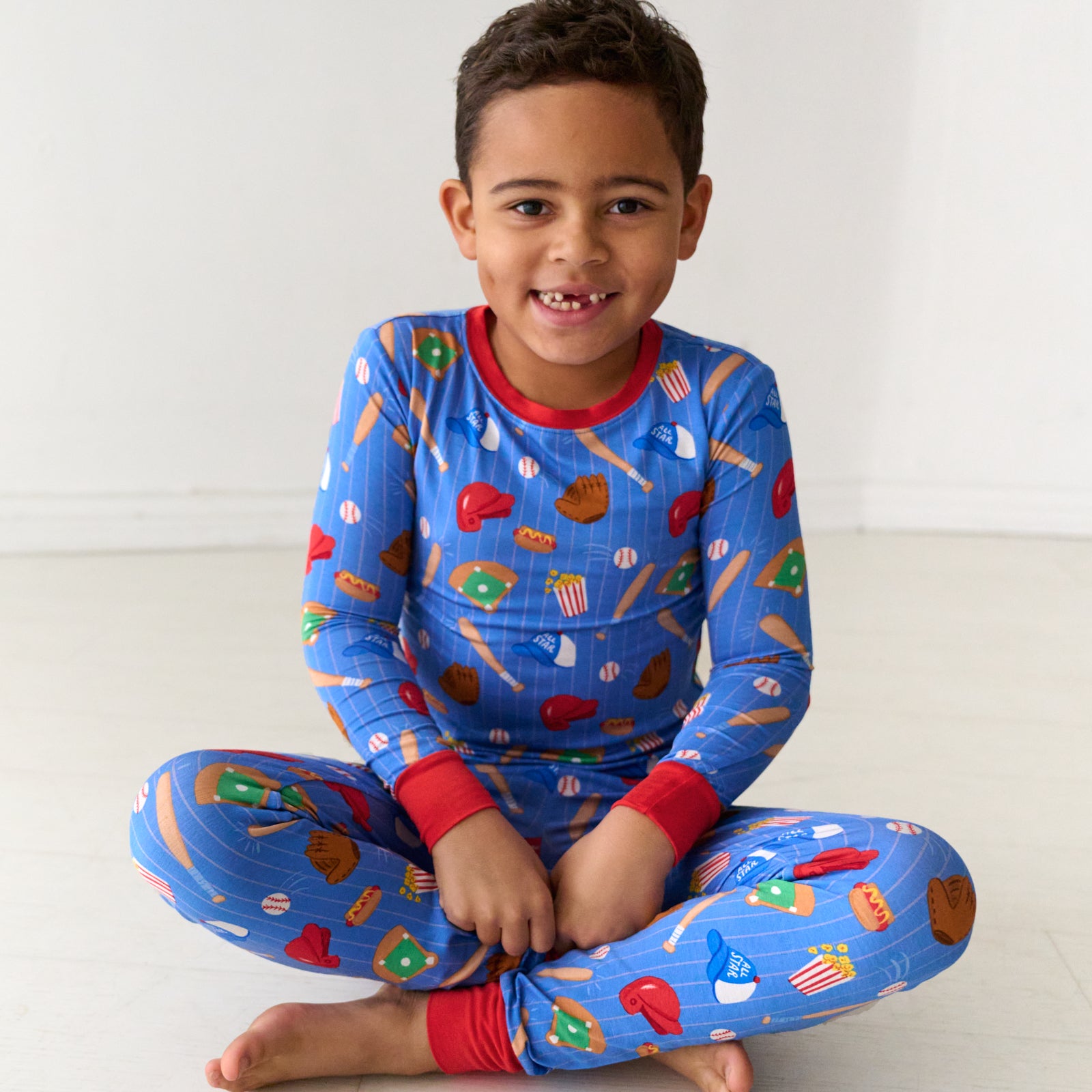 Child sitting wearing a Blue All Stars printed two piece pajama set