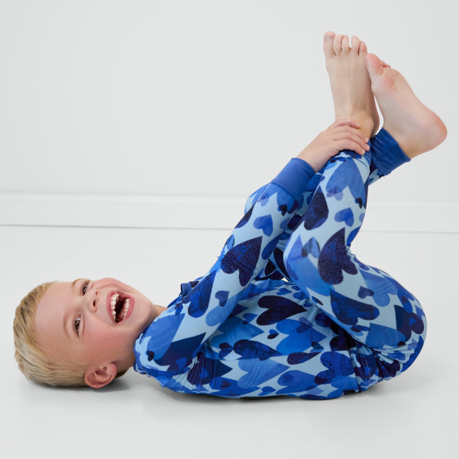 Boy laying down wearing Blue Hearts & Crafts two-piece long sleeve and pants pajama set.