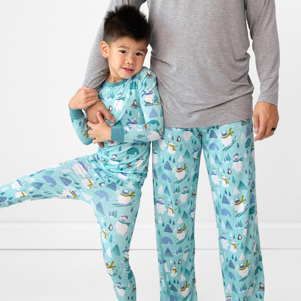 Close up image of a dad wearing a men's Heather Gray pj top and men's Yeti Snow Day pj pants. His son is wearing a matching two piece pj set