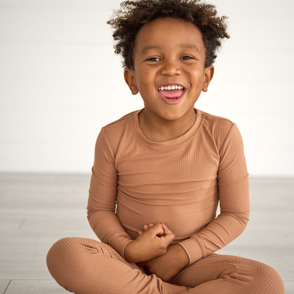 Boy sitting and smiling while in the Caramel Ribbed Two-Piece Pajama Set