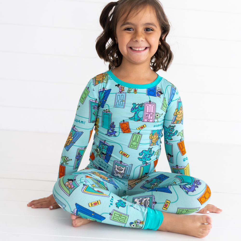 Smiling girl sitting down while wearing the Disney Monsters, Inc. Scream Team Two-Piece Pajama Set