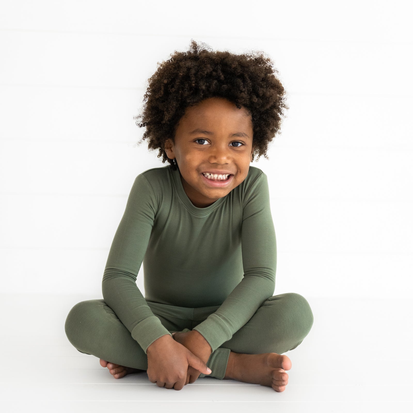 Child sitting wearing a Cozy Olive two piece pajama set