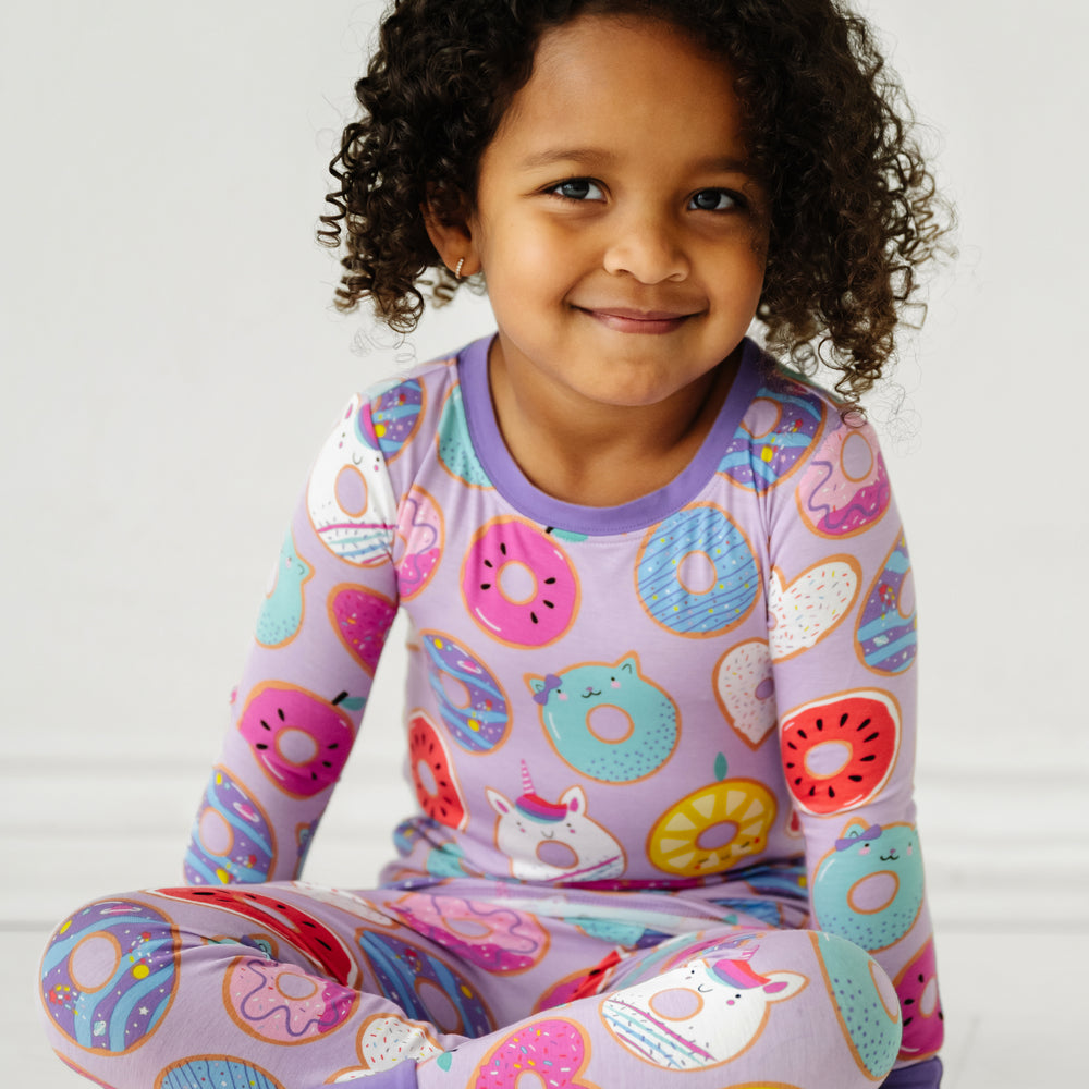 Click to see full screen - Close up image of a child sitting wearing a Lavender Donut Dreams two piece pajama set
